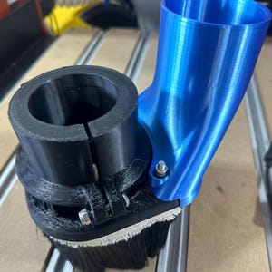 Könnte beinhalten: Ein blauer Staubabsaugaufsatz aus Kunststoff für eine Fräse, mit einer schwarzen Kunststoffklemme und einer Bürste zum Entfernen von Staub.