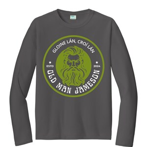 Op de afbeelding: Een donkergrijs longsleeve t-shirt met een groene cirkelvormige afbeelding. De afbeelding toont het gezicht van een man met een baard met de tekst "Old Man Jameson" en "Gloine Lán, Croí Lán" rond de buitenkant. De tekst "Estd 2024" staat onderaan de cirkel.