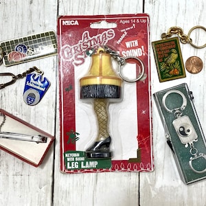 May include: A collection of keychains, including a "Leg Lamp" from "A Christmas Story" with sound, a German Schützenbund keychain, and a Yin Yang keychain. Other keychains feature various designs and a tie clip.