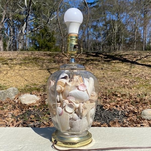 May include: A clear glass table lamp with a gold base. The lampshade is made of seashells.