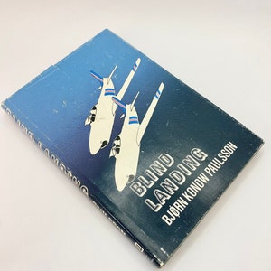 May include: A blue book with a white and blue illustration of two airplanes on the cover. The title of the book is "Blind Landing" and the author is "Bjorn Konow Paulsson".