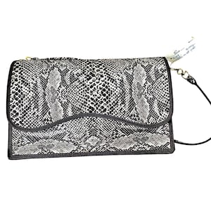 May include: A rectangular handbag with a snakeskin pattern in black and white. The bag has a black border and a gold zipper. A black strap is attached to the bag. A tag is attached to the bag with handwritten text.