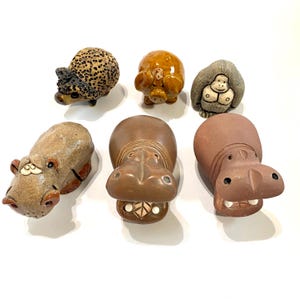 May include: A collection of six ceramic animal figurines. The figurines include a hedgehog with a spotted pattern, a pig, a gorilla, and three hippos. The hippos are brown and tan, with open mouths and detailed features.