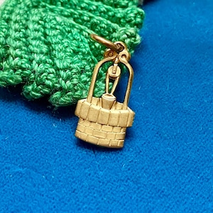 Puede incluir: Un amuleto de color dorado en forma de pozo con un cubo colgando de una polea. El amuleto está detallado con ladrillos y una cuerda.