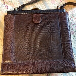 May include: A brown leather handbag with a textured, scaly pattern. The bag has a flap closure with a metal clasp and a long strap.