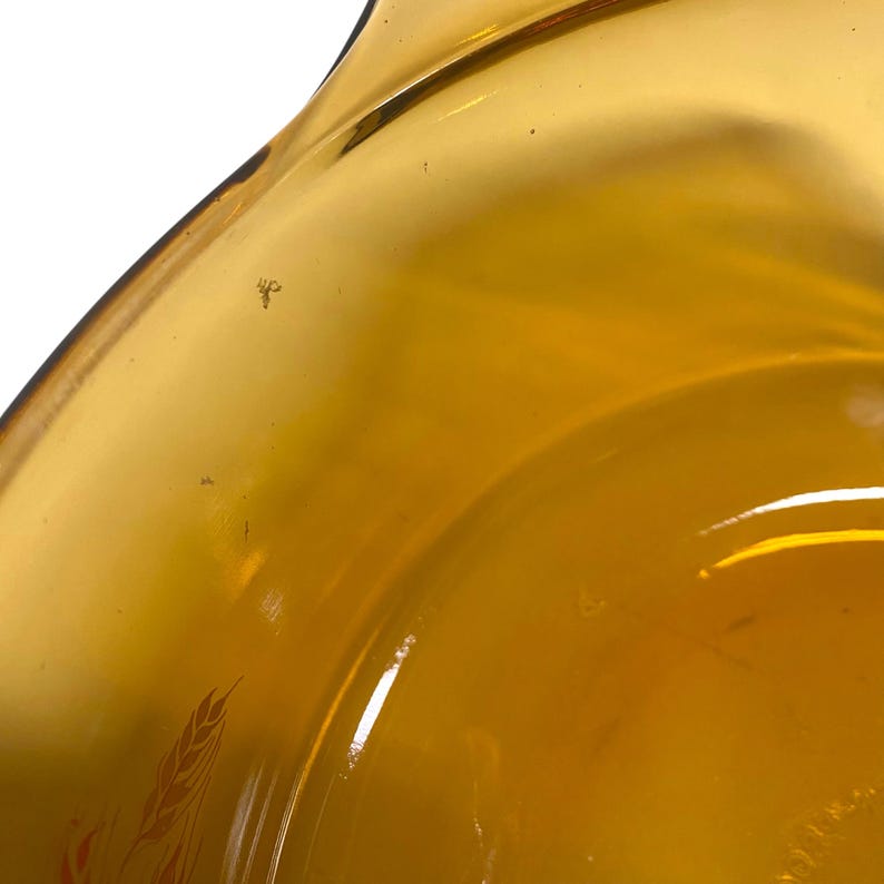 K&ouml;nnte beinhalten: Nahaufnahme einer Vintage-Sch&uuml;ssel aus bernsteinfarbenem Glas. Die Sch&uuml;ssel hat ein geschwungenes Design mit einem Weizenmuster in Orange- und Rott&ouml;nen. Das Glas hat eine gl&auml;nzende Oberfl&auml;che und ist leicht transparent.