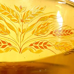 K&ouml;nnte beinhalten: Nahaufnahme einer gelben Glasschale mit einem Weizenmuster. Das Weizenmuster ist in Orange- und Gelbt&ouml;nen gehalten. Die Schale hat eine gl&auml;nzende Oberfl&auml;che und eine leicht gebogene Form. Das Design ist auf der Schale zentriert.