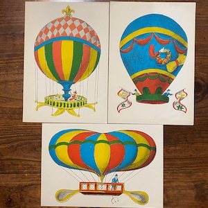 May include: Three vintage hot air balloon illustrations. The balloons are in various colours, including red, yellow, blue, and orange. Each balloon has a unique design, with intricate details and decorative elements. The illustrations are on white paper.