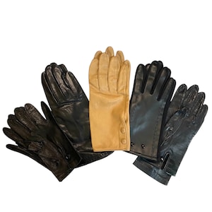 May include: Five leather gloves in various shades of black and tan are displayed against a white background. The gloves have different designs, including button details and decorative stitching. The gloves are likely for cold weather.