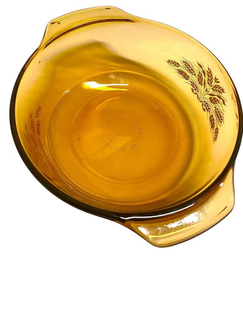K&ouml;nnte beinhalten: Bernsteinfarbene Glasauflaufform mit zwei Griffen. Die Sch&uuml;ssel hat ein Weizenmuster an der Seite. Die Sch&uuml;ssel ist rund und hat eine glatte Oberfl&auml;che. Ein Vintage-K&uuml;chenartikel.