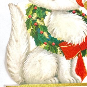 Puede incluir: Una tarjeta de Navidad vintage con un gato blanco con pelaje esponjoso. El gato lleva una corona festiva de acebo verde con bayas rojas y un gran lazo rojo. La tarjeta tiene un borde dorado.