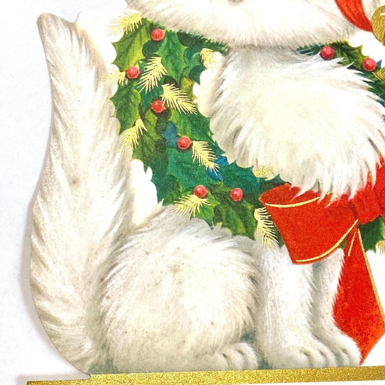 Puede incluir: Una tarjeta de Navidad vintage con un gato blanco con pelaje esponjoso. El gato lleva una corona festiva de acebo verde con bayas rojas y un gran lazo rojo. La tarjeta tiene un borde dorado.
