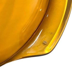 K&ouml;nnte beinhalten: Nahaufnahme eines Teils einer durchsichtigen, bernsteinfarbenen Glasschale. Die Schale hat eine abgerundete Form mit einem leicht erh&ouml;hten Rand. Das Glas hat eine glatte, gl&auml;nzende Oberfl&auml;che mit kleinen Unvollkommenheiten.