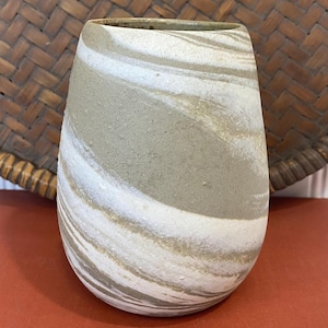 以下が含まれることがあります： ユニークなデザインの手作りセラミック花瓶。花瓶は、渦巻く白とタンのストライプが入った明るい灰色のベースが特徴です。花瓶はわずかにフレアした上部と滑らかで質感のある表面を持っています。花瓶は装飾品です。