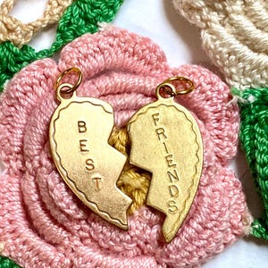 以下が含まれることがあります： 「BEST」と「FRIENDS」が刻まれた、2つの金色のハート型のチャーム。チャームは半分に割れており、ペアで着用することを示唆している。
