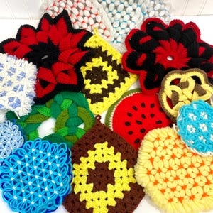 May include: A collection of colorful, handmade crochet pot holders in various shapes and designs. The pot holders feature a variety of colors, including red, black, yellow, green, and blue. Some are shaped like flowers, squares, and a watermelon slice.