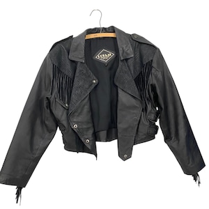 Puede incluir: Chaqueta de cuero negra con detalles de flecos en los hombros y las mangas. La chaqueta tiene cierre de cremallera y cuello con botón a presión. La etiqueta dice "Leeann's Leather Creations".