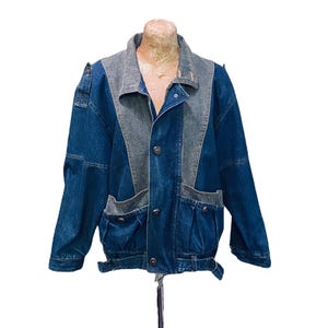 May include: A blue denim jacket with a contrasting grey denim panel on the front and a belt at the waist.