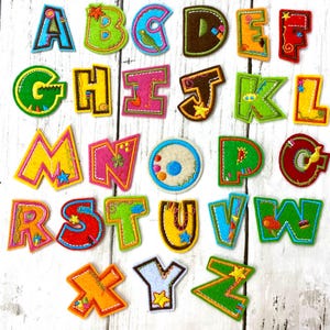 May include: A collection of colorful, felt alphabet letters in various colors, including green, blue, yellow, and pink. Each letter is uniquely designed with decorative stitching and embellishments, perfect for crafting or educational projects.
