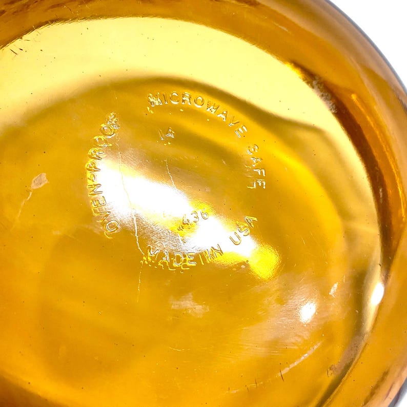 K&ouml;nnte beinhalten: Nahaufnahme des Bodens einer gold-bernsteinfarbenen Glasschale. Der Text "OVEN-PROOF", "MICROWAVE SAFE" und "MADE IN USA" sind sichtbar. Die Nummer "436" ist ebenfalls auf dem Glas aufgedruckt.