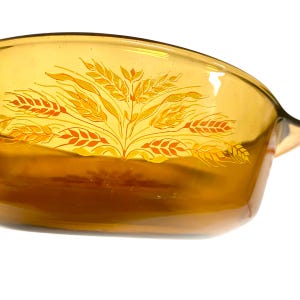 K&ouml;nnte beinhalten: Bernsteinfarbene Backform aus Glas mit einem Weizen&auml;hren-Design. Die Form hat eine rechteckige Form mit abgerundeten Ecken und einem Griff auf einer Seite. Das Weizendesign ist in Gelb- und Oranget&ouml;nen gehalten.