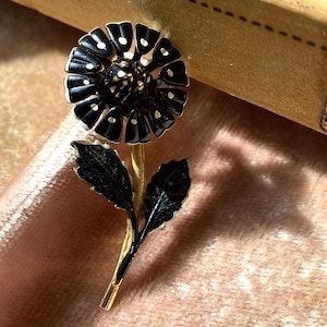 May include: A black and white enamel flower brooch with gold-tone stem and leaves.