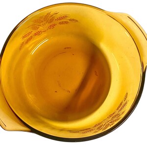 K&ouml;nnte beinhalten: Bernsteinfarbene Glas-Auflaufform mit Weizenmuster. Die Form hat zwei Griffe und eine abgerundete Form. Das Weizenmuster ist in dunklerem Bernstein gedruckt. Wahrscheinlich Vintage, zum Backen oder Servieren.