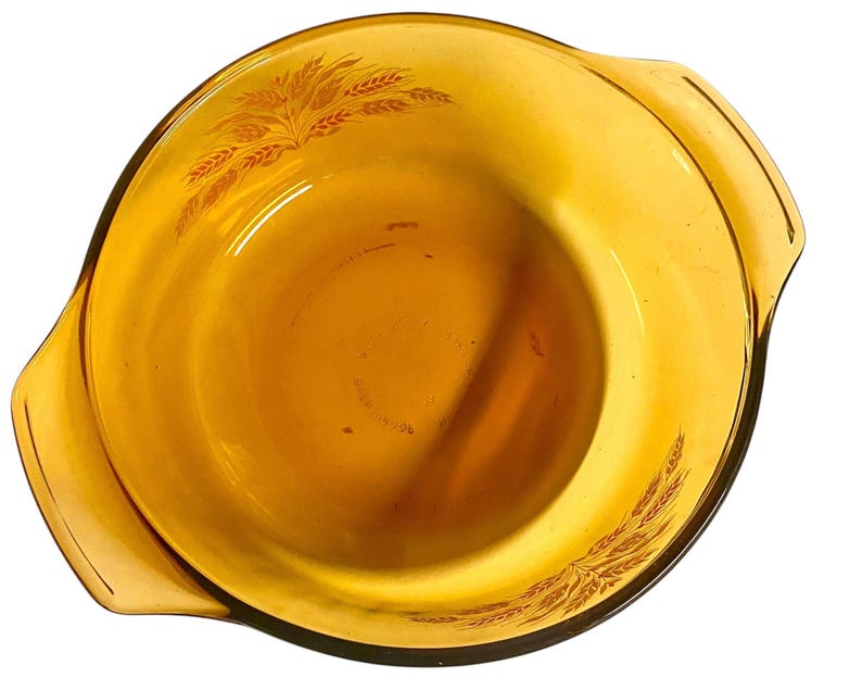 K&ouml;nnte beinhalten: Bernsteinfarbene Glas-Auflaufform mit Weizenmuster. Die Form hat zwei Griffe und eine abgerundete Form. Das Weizenmuster ist in dunklerem Bernstein gedruckt. Wahrscheinlich Vintage, zum Backen oder Servieren.