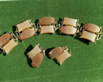 Puede incluir: Una pulsera de eslabones dorados y un par de pendientes de clip a juego, cada uno con piezas rectangulares opacas de color beige claro y cabujones ovalados de color marrón oscuro en monturas de metal pulido.