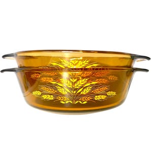 K&ouml;nnte beinhalten: Zwei bernsteinfarbene Auflaufformen aus Glas mit einem Weizen&auml;hren-Design in Gelb- und Oranget&ouml;nen. Jede Form hat schwarze Griffe. Die Formen sind gestapelt. Ma&szlig;e in Zentimetern.