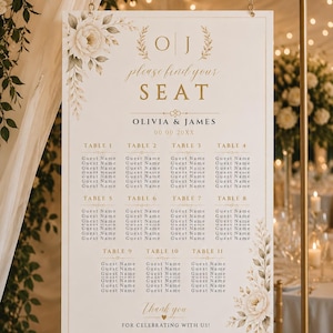 Puede incluir: Un cartel rectangular de distribución de mesas de boda con fondo blanco y texto dorado. Presenta las iniciales O J, el texto please find your SEAT, OLIVIA & JAMES, y listas para las mesas 1 a 11. El diseño incluye ilustraciones florales.