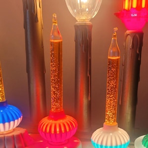 Può includere: Una collezione di luci a bolle natalizie vintage. Ogni luce presenta un tubo di vetro trasparente riempito con un liquido che bolle quando riscaldato. Le basi sono di vari colori, tra cui blu, rosa, bianco e verde.