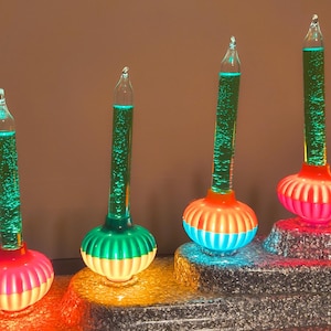 May include: Four bubble lights featuring clear glass tubes filled with green liquid and rising bubbles. Each light has a ribbed, colorful base in shades of pink, green, orange, and blue, arranged in a stepped formation.