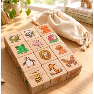 May include: A set of wooden blocks featuring colourful illustrations of animals including a panda, flamingo, frog, lion, penguin, bee, giraffe, and butterfly, accompanied by a beige drawstring storage bag and a book titled Little Explorers Wild Animals.