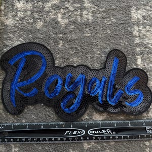 May include: A black and blue sequined patch with the word "Royals" in blue sequins.