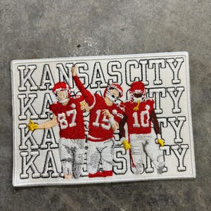 May include: Embroidered patch featuring three football players in red uniforms with the text "KANSAS CITY" repeated four times in white.