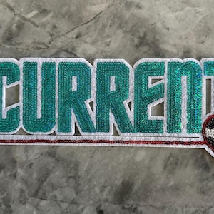 May include: A white patch with the word "CURRENT" in teal sequins and a red heart with a black and white soccer ball design.