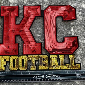 May include: A large fabric patch featuring the red sequined letters KC above the gold sequined word FOOTBALL. A yellow measuring tape on the left shows a height of 9 inches, and a black ruler at the bottom shows a width of 11 inches.
