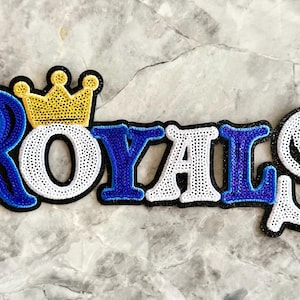 May include: A blue, white, and gold embroidered patch with the word "ROYALS" and a crown above the "O".