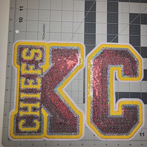 May include: Two sequined patches. One patch spells out "CHIEFS" in yellow letters with a red sequined background. The other patch is a red sequined "C" with a yellow border. Both patches have a white border.