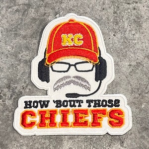 May include: White embroidered patch with a cartoon of a person wearing a red baseball cap with the letters "KC" in yellow, glasses, a mustache, and a headset. The text "HOW 'BOUT THOSE CHIEFS" is below the cartoon in red and yellow letters.