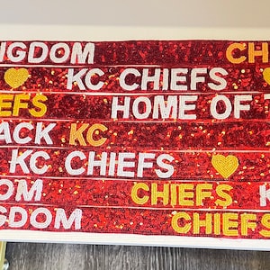 May include: Red and gold sequined ribbon with the text "Chiefs Kingdom", "Chiefs", "KC Chiefs", "Home of the Chiefs", "Run it Back KC", and "Chiefs Kingdom" repeated.