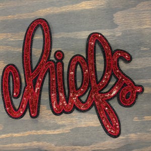 May include: Red and black sequined iron-on patch that says "chiefs" in a cursive font.