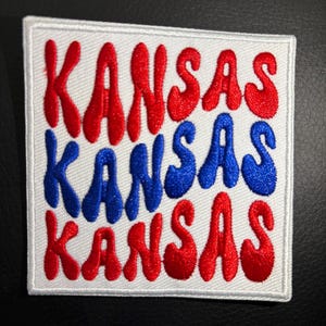 May include: White patch with the word "Kansas" written three times in red and blue lettering. The letters are stylized and have a rounded, bubbly appearance.