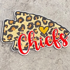 May include: Embroidered patch in the shape of an arrow with a leopard print pattern. The word "Chicks" is embroidered in red script, with a small gold heart. The patch has a white border.