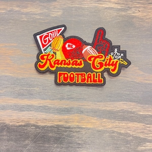 May include: Embroidered patch with a red, white, and yellow Kansas City Football design. The patch features a football, a helmet, a trophy, and a hand pointing up. The text "Go Chiefs" is on a red pennant.