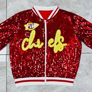 K&ouml;nnte beinhalten: Rote Pailletten-Bomberjacke mit wei&szlig;-roten Streifen. Mit dem Text "Chiefs" in gelber Schrift und einem "KC"-Logo. Die Jacke hat einen durchgehenden Rei&szlig;verschluss und einen wei&szlig;en Kragen.