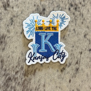 May include: White embroidered patch with a blue "K" inside a shield with a gold crown and the text "Long Live the K" above it. The text "Kansas City" is below the shield.