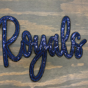 May include: Blue and black sequined applique of the word "Royals".