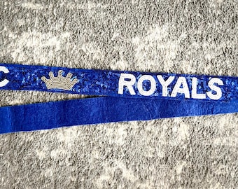 May include: Blue and white sequined strap with gold hardware and the text "KC ROYALS" with a crown on each side.